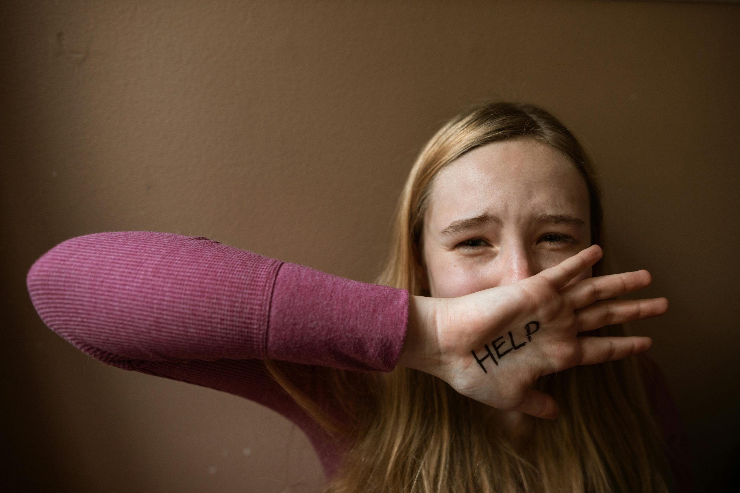 Young woman victim of domestic violence with Help written on her hand. Intimate partner violence also includes elder abuse.