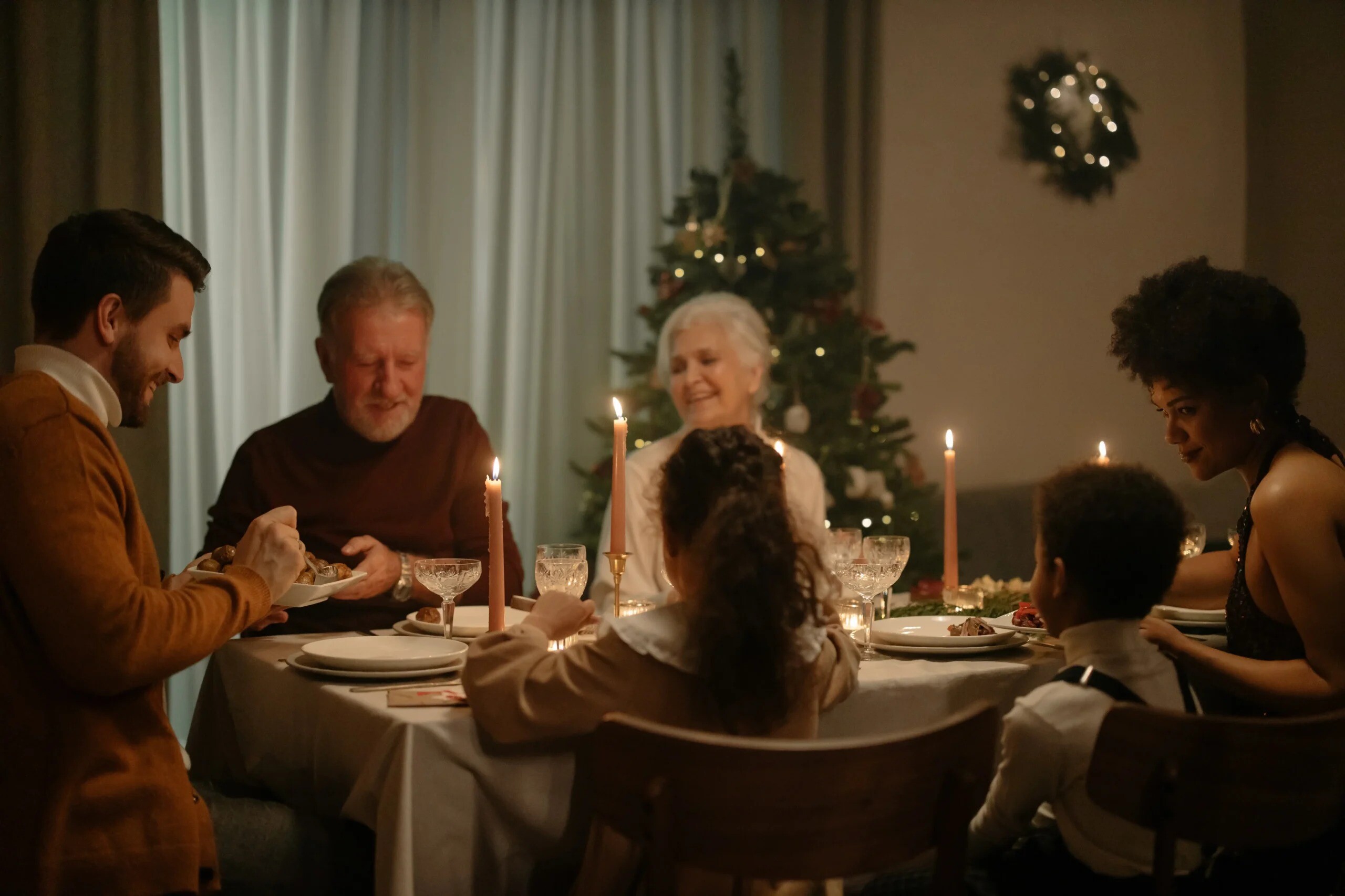 Multigenerational family gathered around a dinner table at Christmas time, grateful for Life Backup Plan enabling the senior citizens to do aging in place, the caregivers to easily monitor them, and the parents to monitor their young children, too