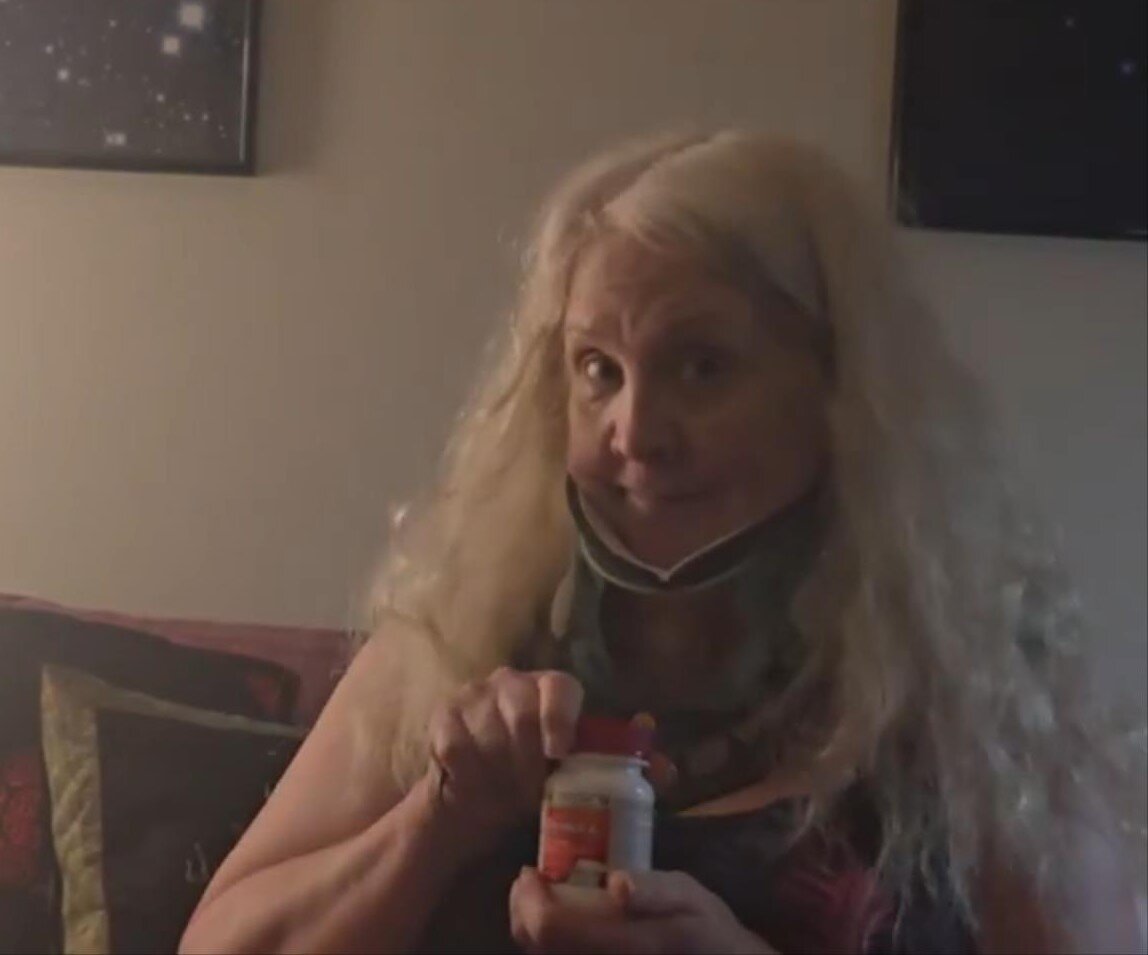 Sandy Eulitt, CEO and Founder of Life Backup Plan by Galacxia, Inc., wearing a cervical hard collar after ACDF (anterior cervical decompression and fusion) and PCDF (posterior cervical decompression and fusion) with rods and screws spine surgery, holding a bottle of Tylenol Muscle Aches & Pain while demonstrating the Life Backup Plan app’s Request Assistance feature for post-discharge monitoring, caregiver alerts, personal health record, and faster intervention while home alone recovering.